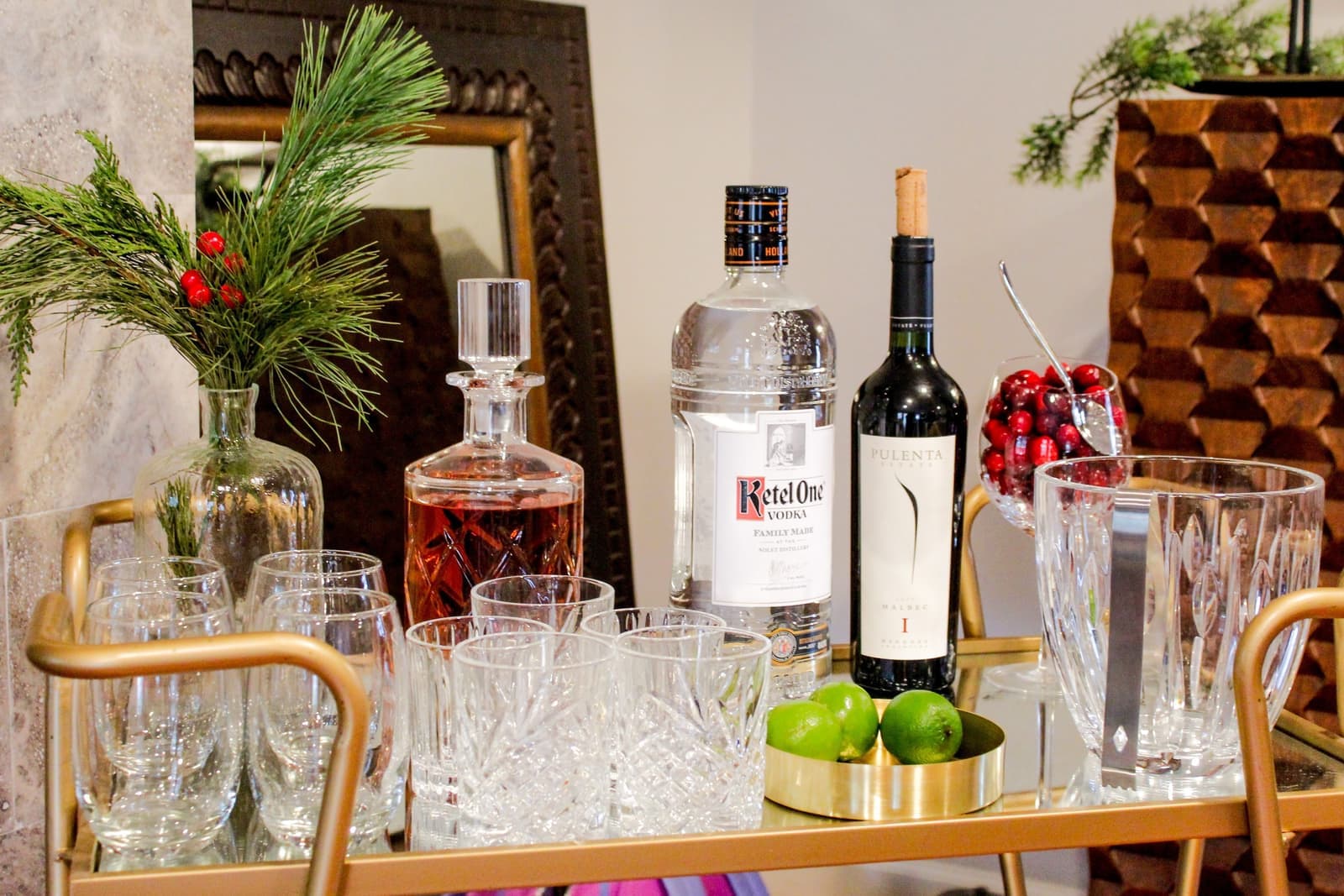 A bar cart holding bottles and glassware standing beside a sofa in a bright room